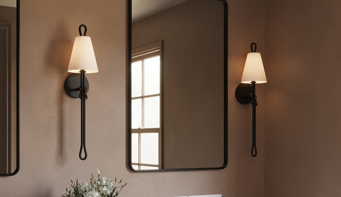 Two Archer 24" tall Wall Sconces in Aged Iron with white fabric shades, shown flanking a black vanity mirror in a bathroom with warm taupe plaster walls.