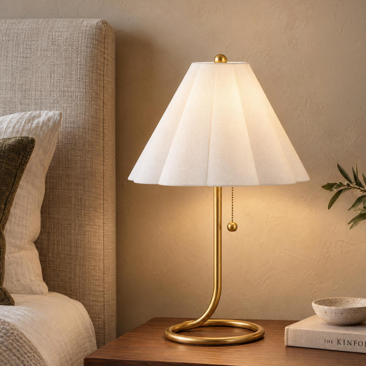 A transitional bedroom with the Nina Table Lamp, Aged Brass resting on a dark wood nightstand next to a neutral upholstered linen headboard.