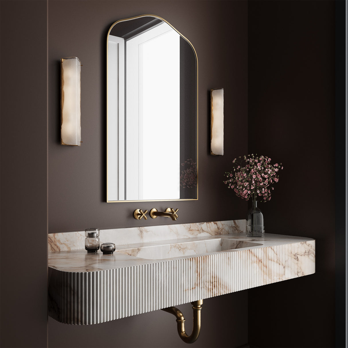 Bathroom vanity with marble countertop, brass mirror, and two Kira Wall Sconces in aged brass on a dark wall.