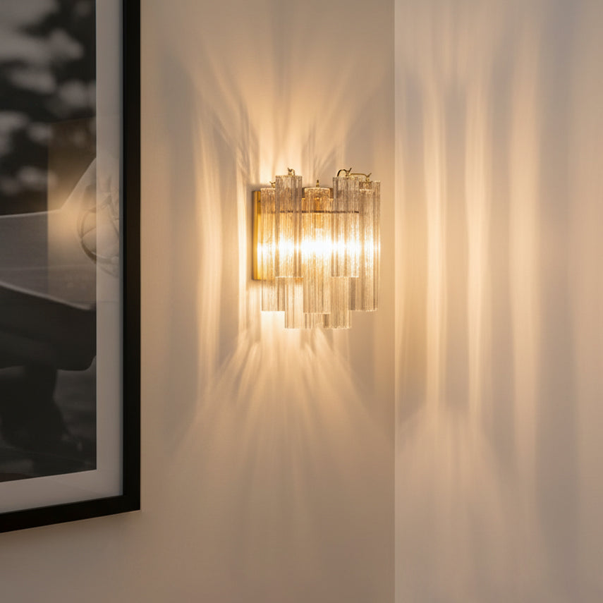 Grace Wall Sconce 14", Brass with Clear Glass, shown on an off-white wall next to a large framed photograph, with brilliant light and shadows projected from the light.