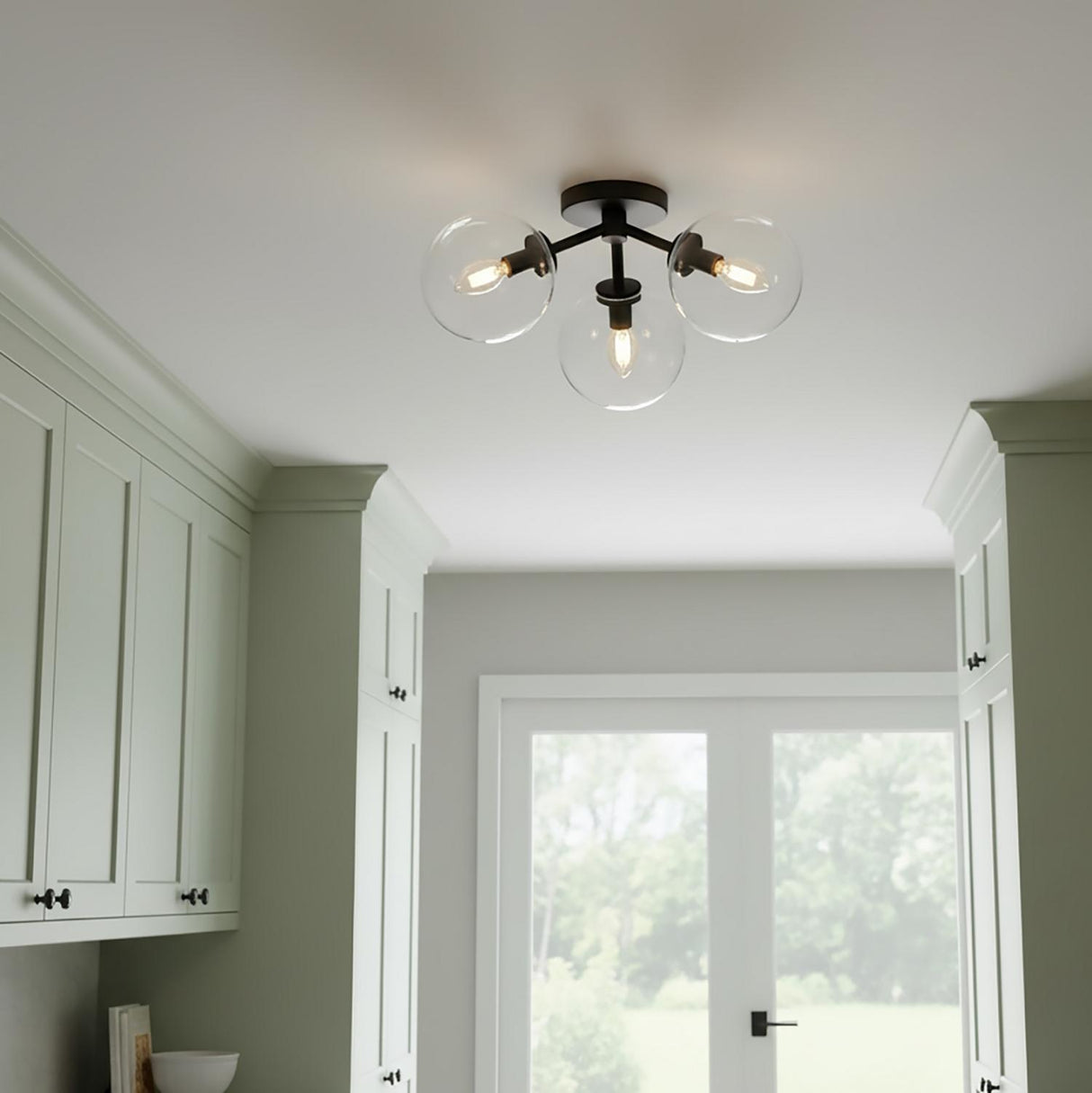 A transitional kitchen space featuring the Gurt 3 Light Semi-Flush 18", Matte Black fixture with clear glass globes along the ceiling center between sage green shaker cabinets.