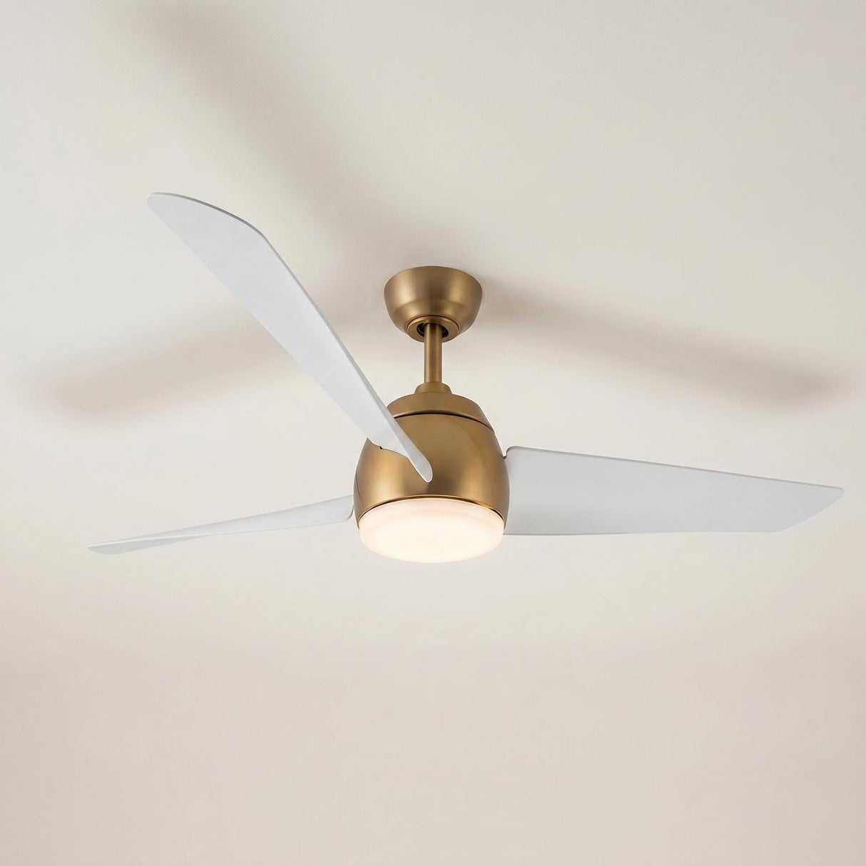 A modern living room with the Lorain LED Ceiling Fan, Brushed Brass and White with three white blades and a frosted glass lens along a flat white ceiling.