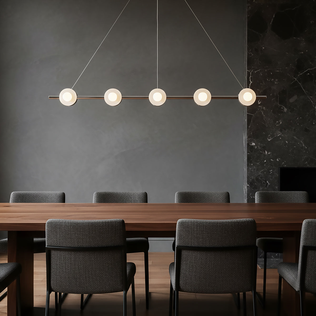 Modern 48" wide pendant light over a long wooden dining table with gray chairs against a dark wall.
