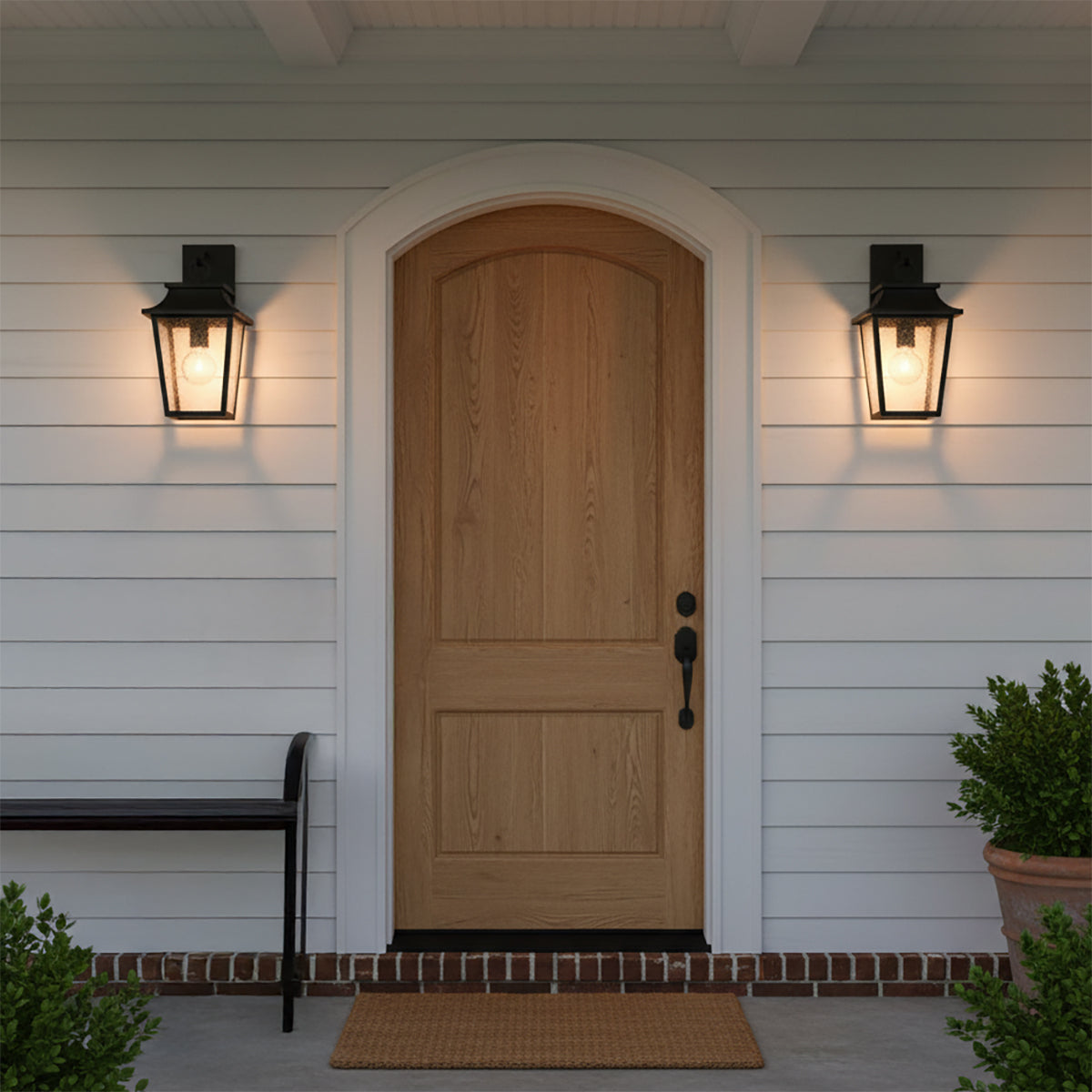 Beckett Outdoor Wall Light, Small 16" Black - Two black lantern-style wall lights flank a natural wood arched door with a doormat and a bench.
