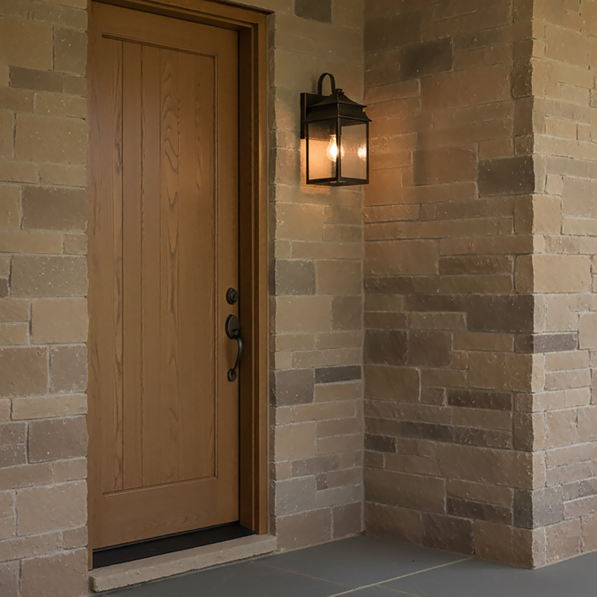 Hanover Outdoor Wall Light, Small 15" in Oiled Bronze finish, shown on a beige stone house next to the front door.