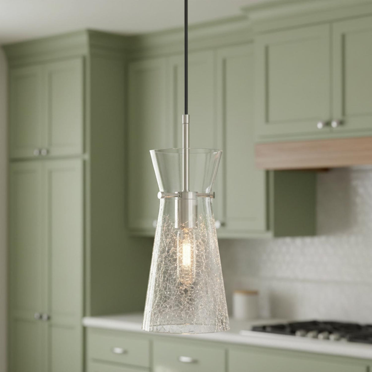 A transitional kitchen features the Aries Pendant 6", Polished Nickel with a crackle glass shade over the island, sage green shaker cabinets, and white tiled backsplash.