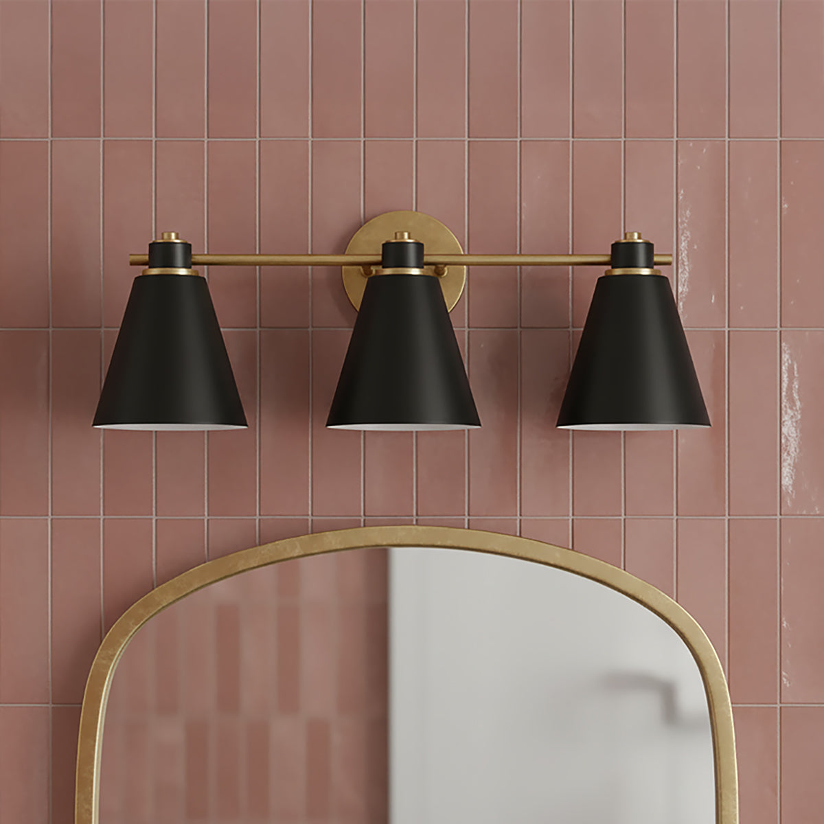 Avin 3 Light Vanity, Matte Black and Aged Brass - A three-light vanity fixture in matte black and aged brass hangs above an arched mirror, mounted on a tiled wall.