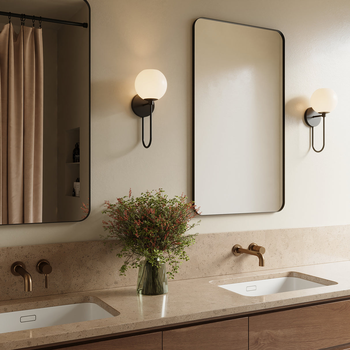 Two Enid Wall Sconces in Matte Black are shown flanking a curved bathroom mirror, above taupe stone countertops and a light wood double vanity.