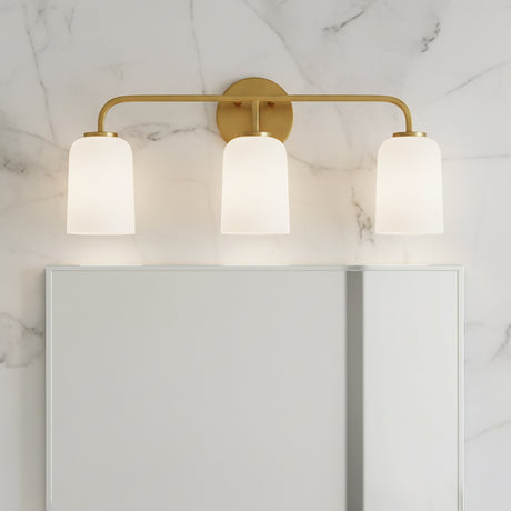 Modern Elira vanity light, in Aged Brass with three white glass shades on a marble wall background.