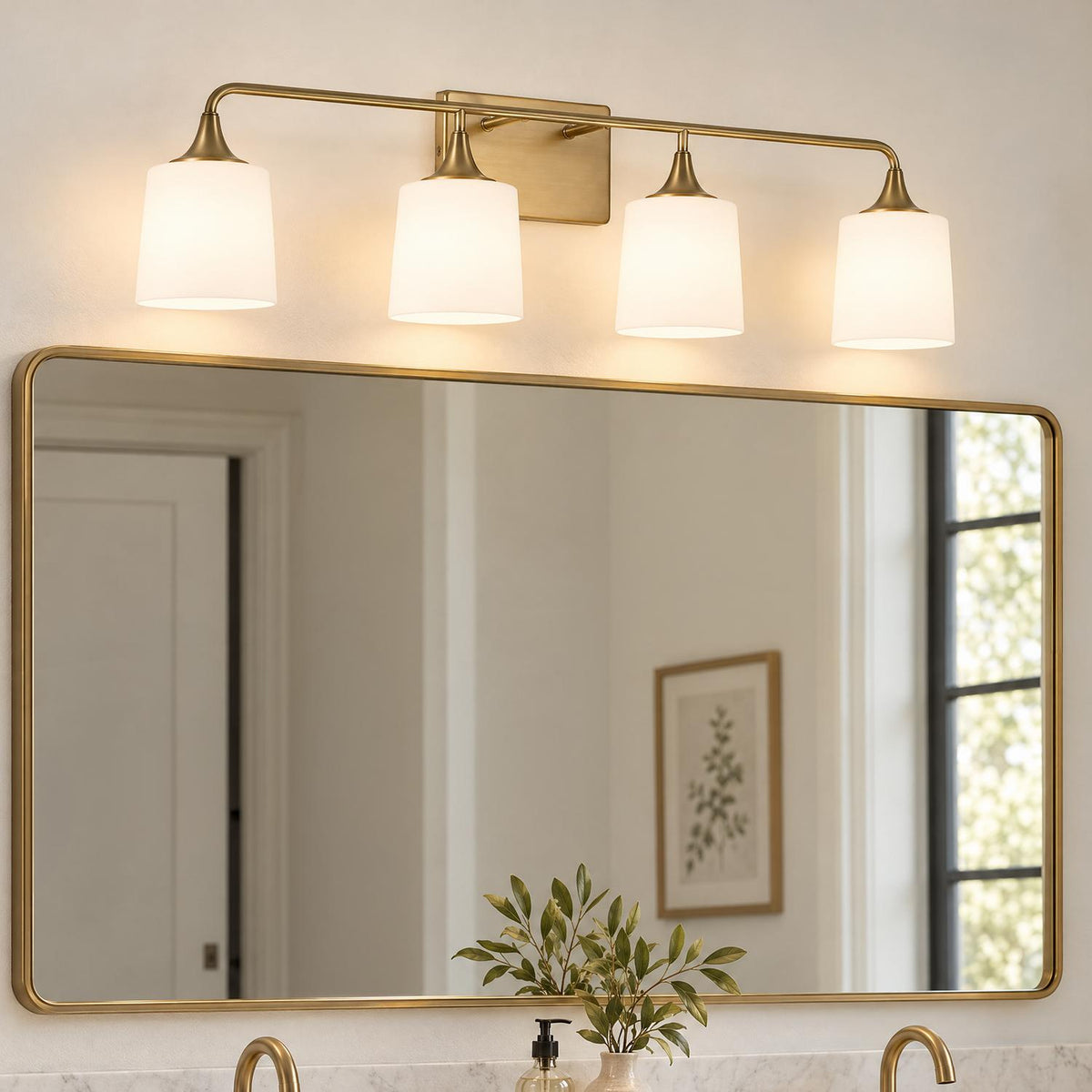 A transitional bathroom features the Harper 4 Light Vanity, Aged Brass with frosted white glass shades installed above a large brass-framed mirror over marble counters.
