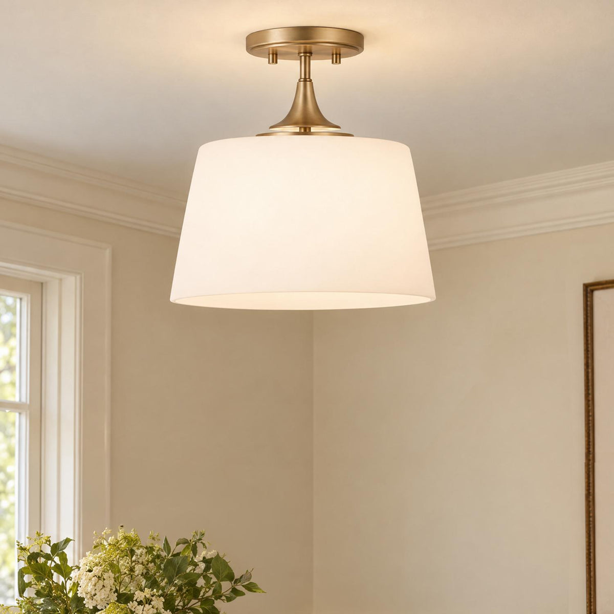 A transitional living room features the Harper Semi-Flush 12, Aged Brass fixture with a white tapered shade, set against white walls with crown molding.