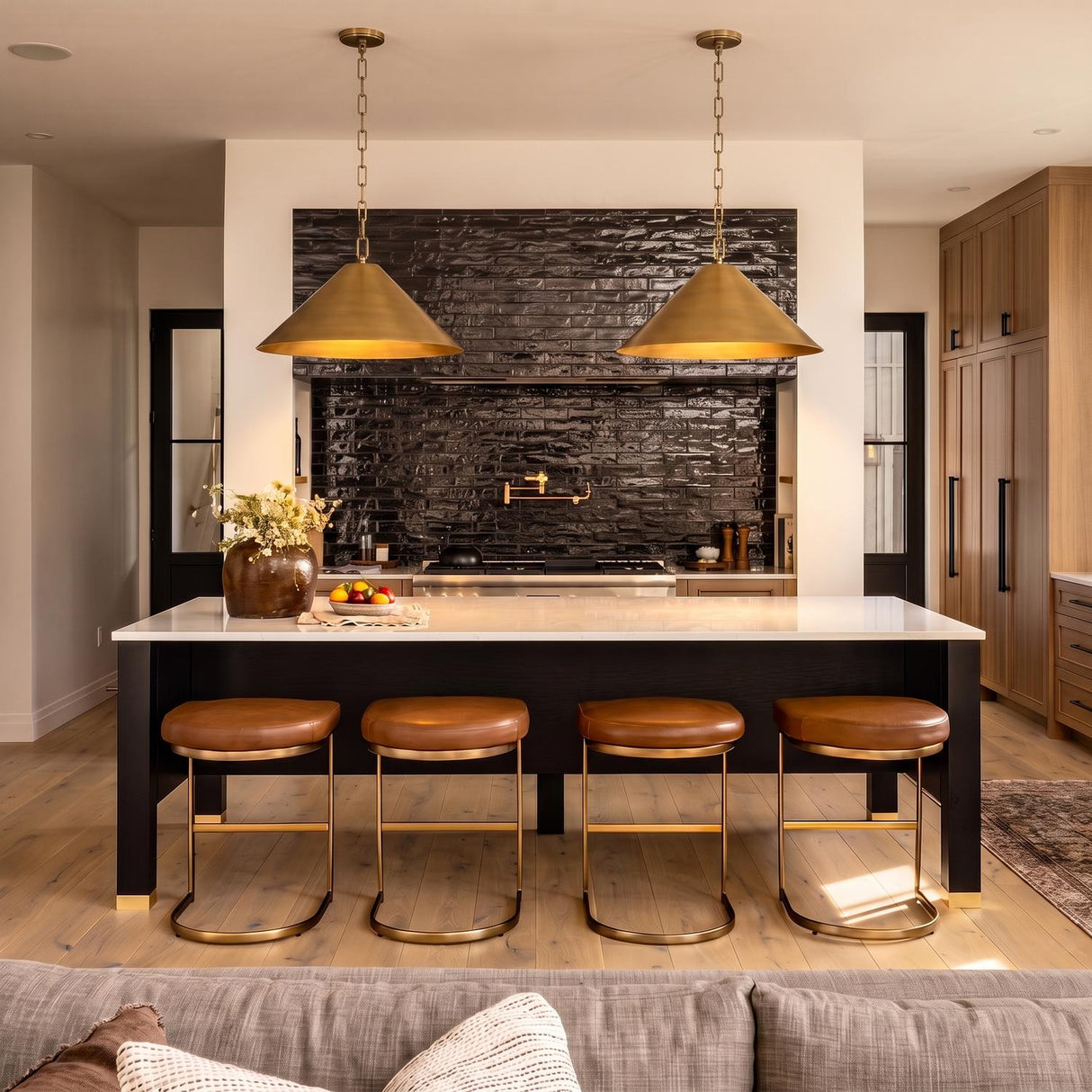 A modern farmhouse kitchen with two aged brass cone pendants over a black island with a white quartz countertop and a textured black backsplash.