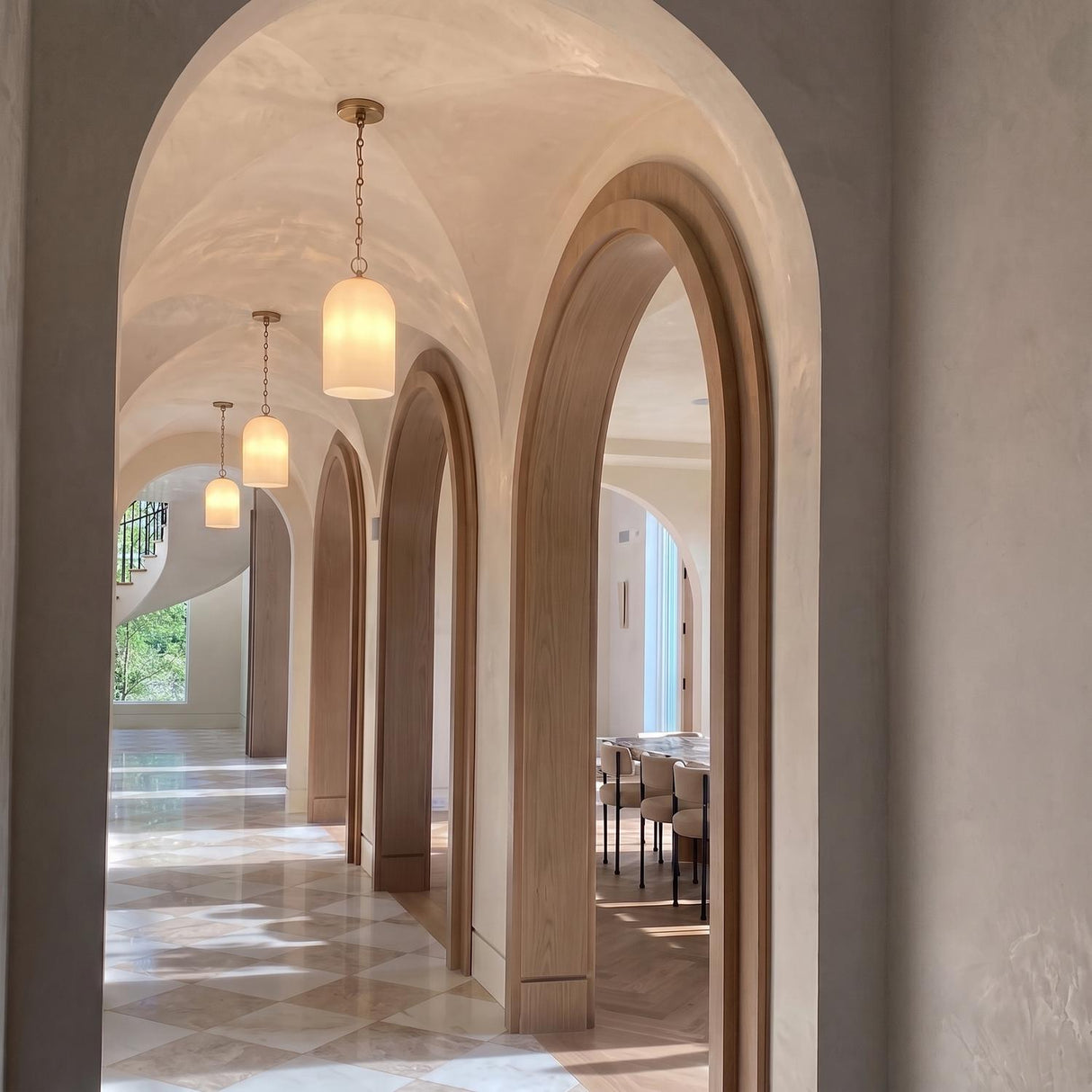 A Mediterranean foyer with three Tovi Pendants in matte brass with cloud opal glass suspended along a groin-vaulted ceiling over diamond-patterned marble tile flooring.