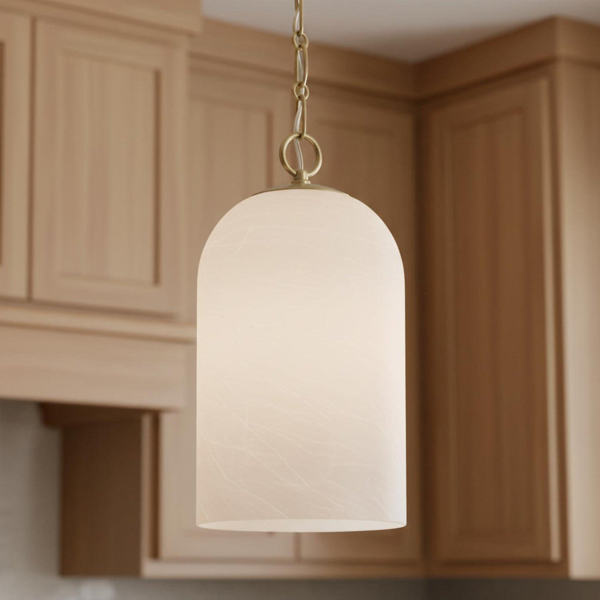 A transitional kitchen features the Tovi Pendant 9" Matte Brass with Cloud Opal Glass suspended over the island, surrounded by light wood shaker style cabinetry.