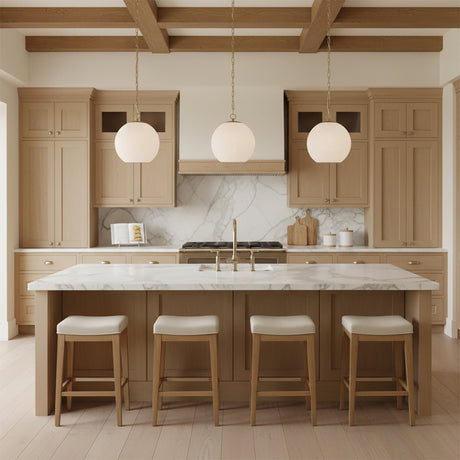 Tova Pendant 14, Matte Brass with Cloud Opal Glass - Three pendant lights with round white glass shades hang over a kitchen island.