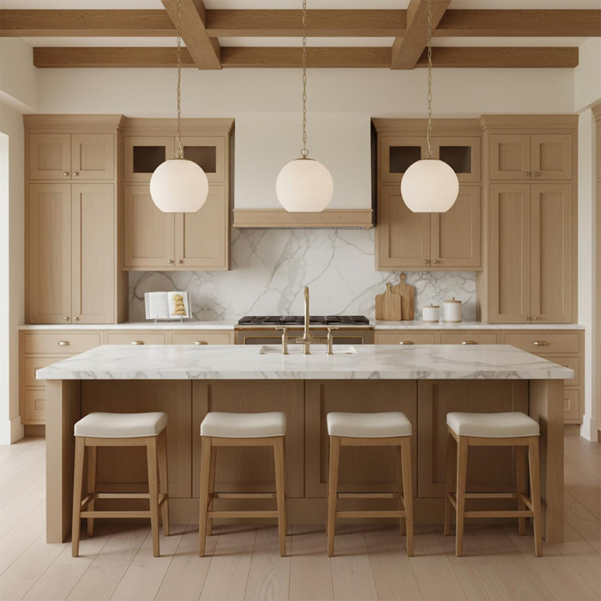 A transitional kitchen features three Tova Pendant 14", Matte Brass with Cloud Opal Glass fixtures over a white marble island under a beamed ceiling with wood cabinets.