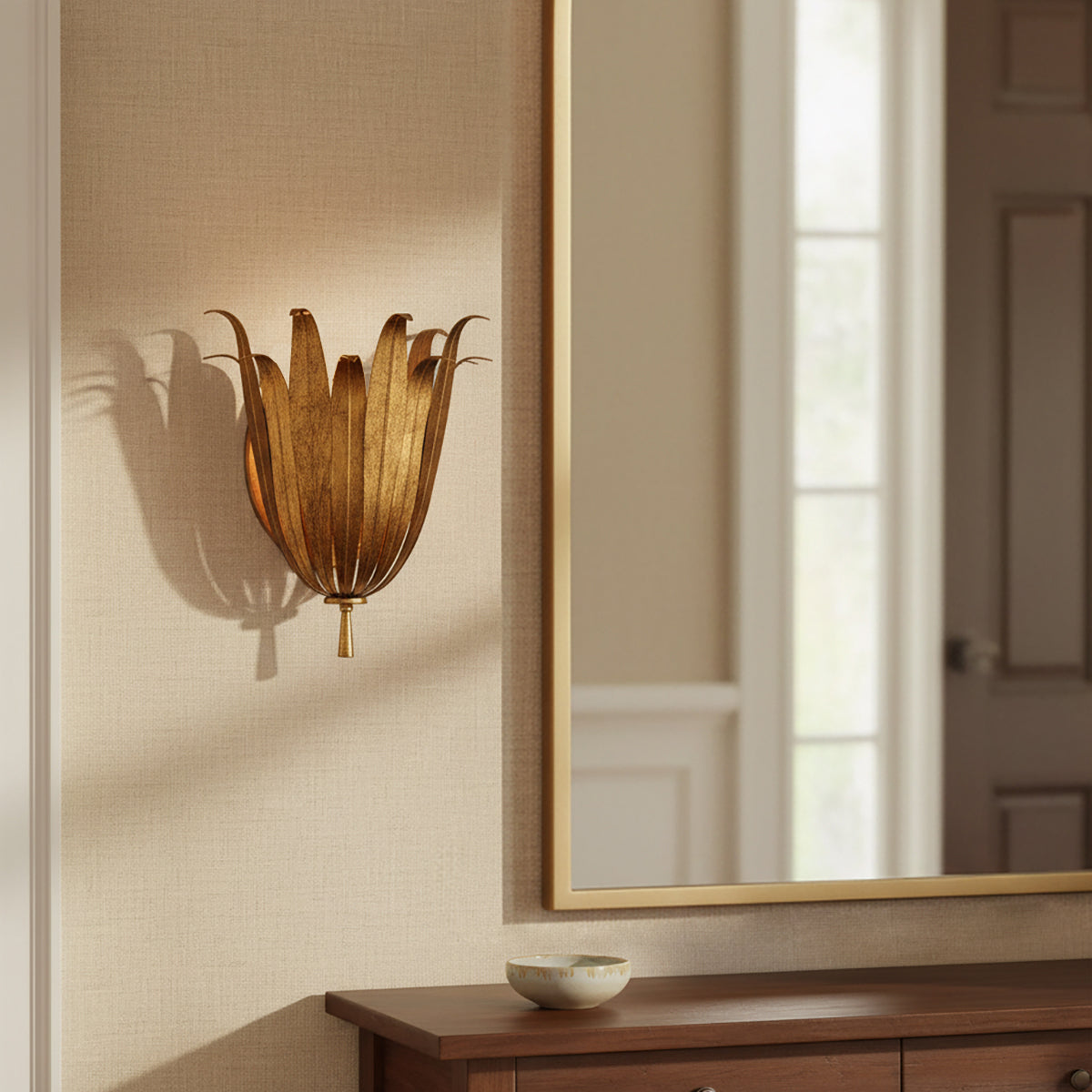 Cerise Wall Sconce 14, Antique Gold - A golden botanical-shaped wall sconce mounted on a textured beige wall next to a gold-framed mirror in the daytime