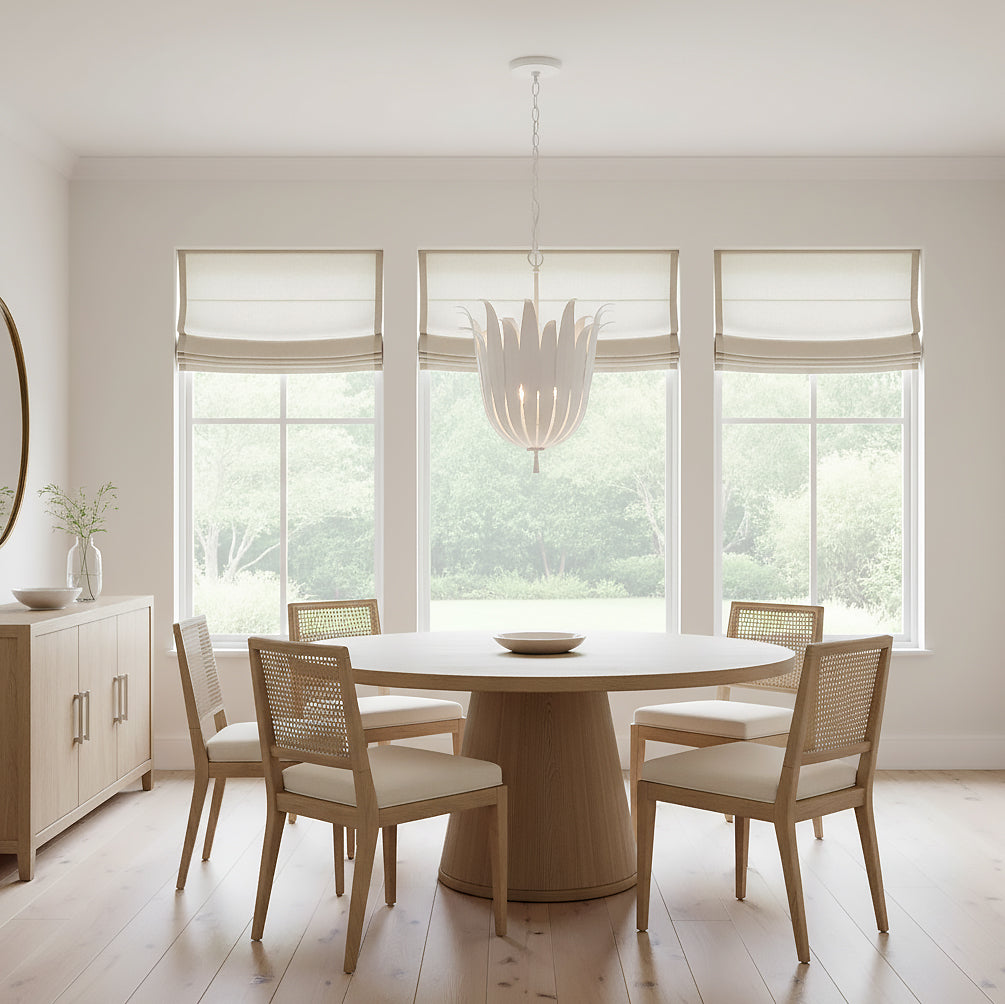 Cerise Pendant 16, Textured White - Pendant light with layered petals hanging over a round wooden dining table with four cane-backed chairs, in a room with large windows looking out to greenery.