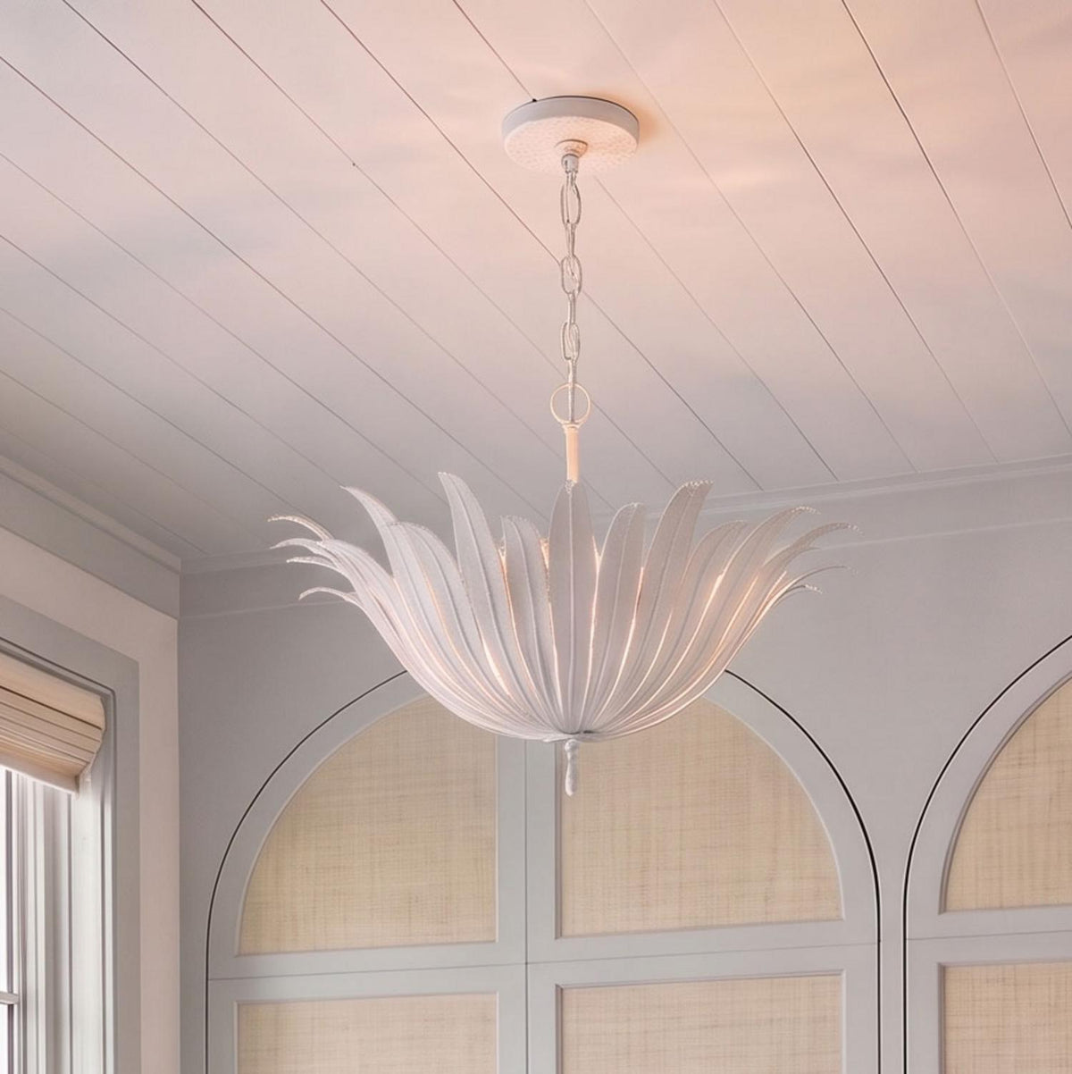 A coastal living room features the Cerise Pendant 24", Textured White suspended from a white shiplap ceiling above arched cane wall paneling.