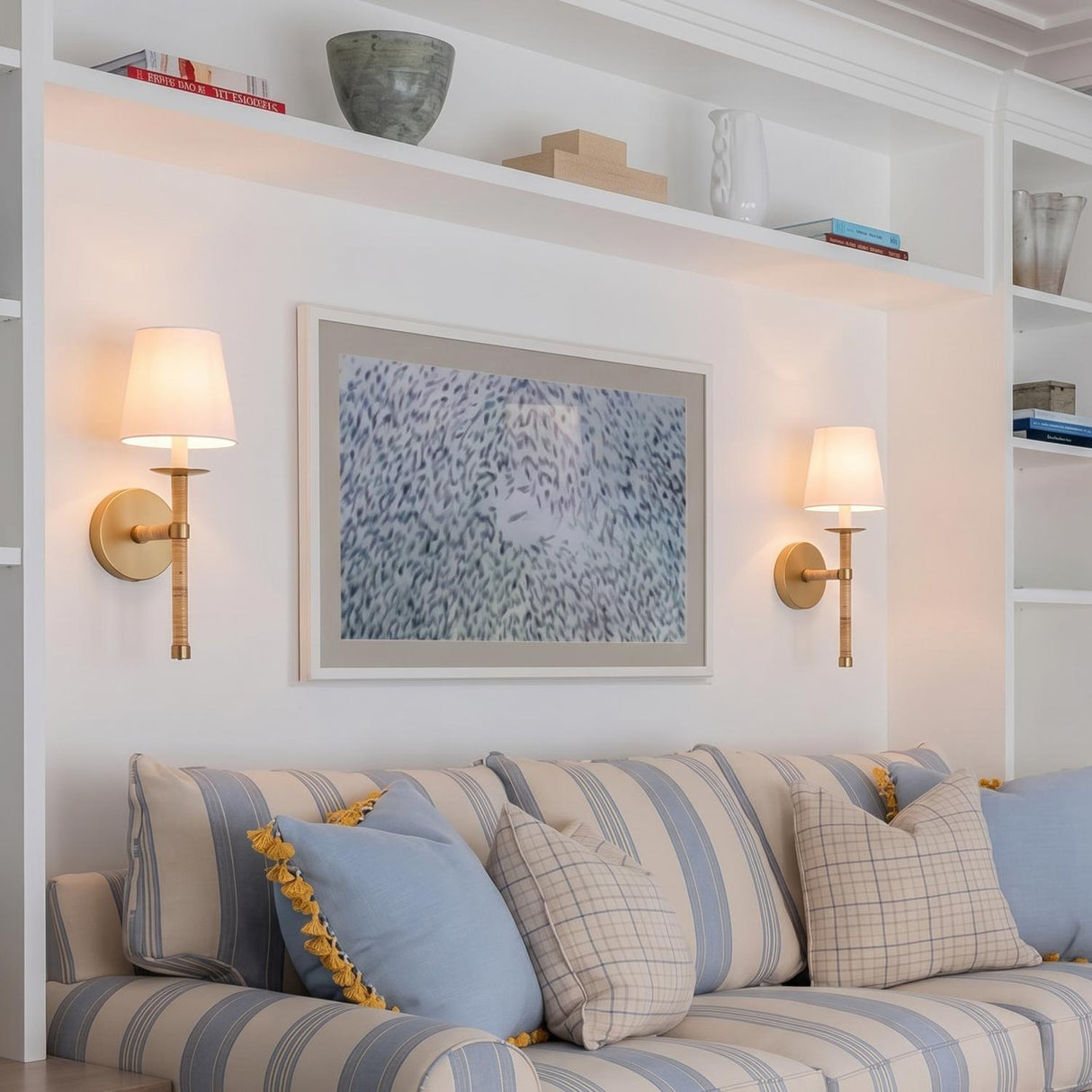 A transitional living room with two Faris Wall Sconce 18" in matte brass with rattan and linen shades flanking artwork above a striped blue sofa.