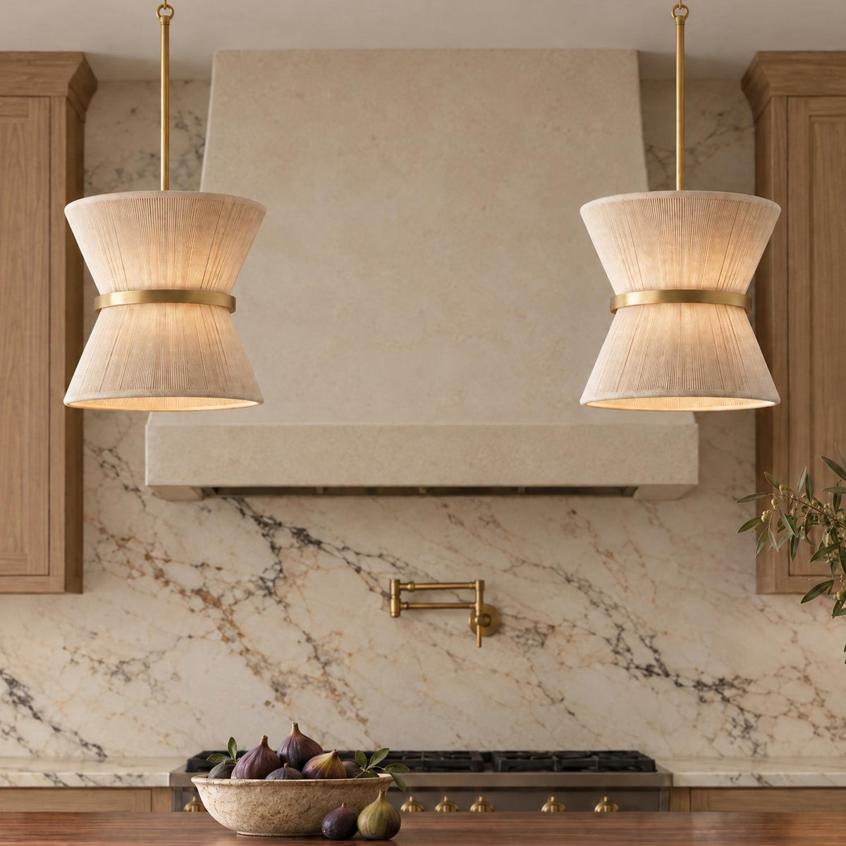 A transitional kitchen with two patina brass and natural rope pendants suspended over a wooden island in front of a marble backsplash and brass pot filler.