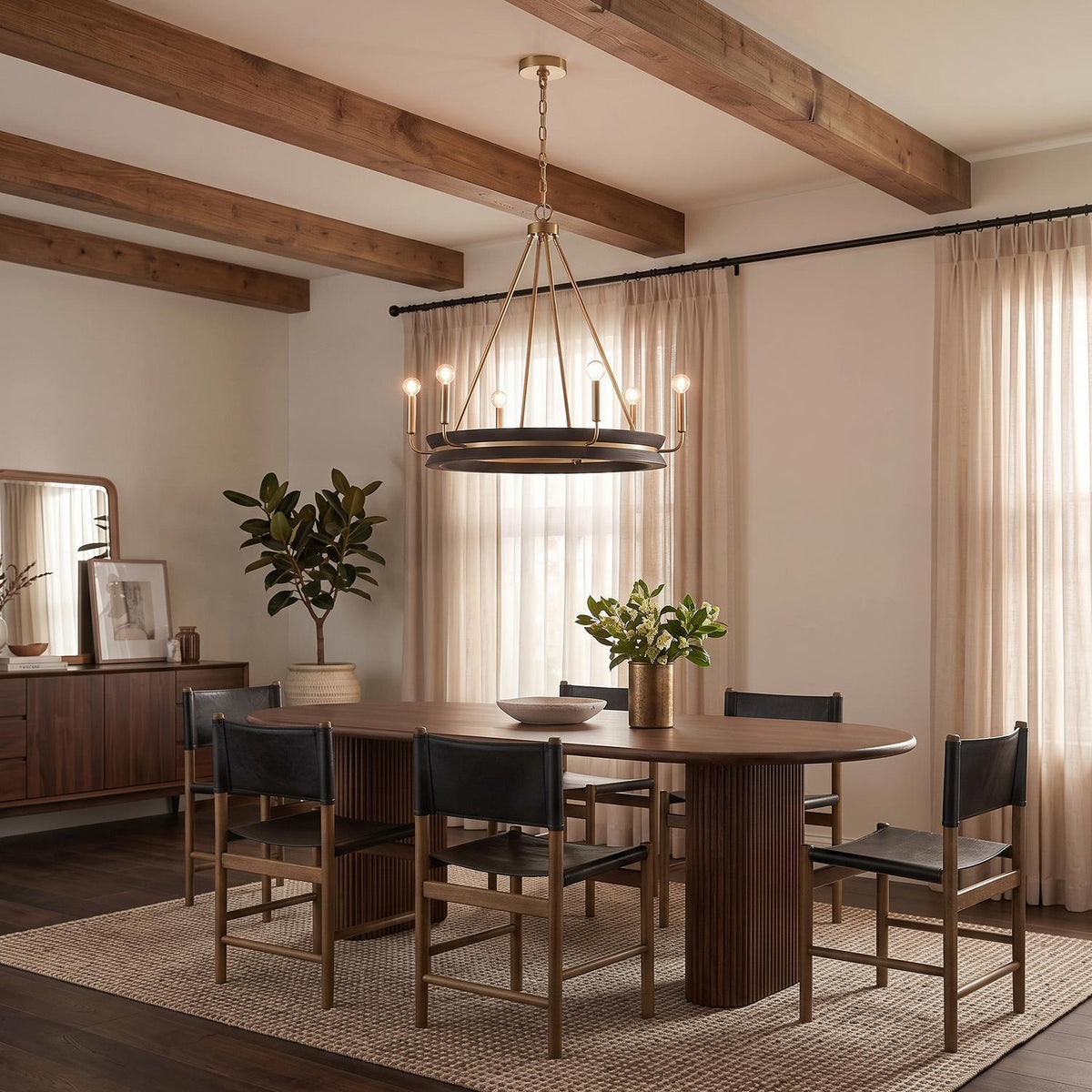 A modern farmhouse dining room featuring the Maren 6 Light Chandelier in ebony and matte brass over a walnut table under a beamed ceiling with beige curtains.