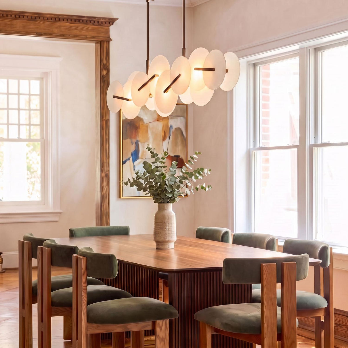 A contemporary dining room with the Malya LED Linear Chandelier in brass with opal glass suspended over a dark wood dining table and green upholstered chairs.