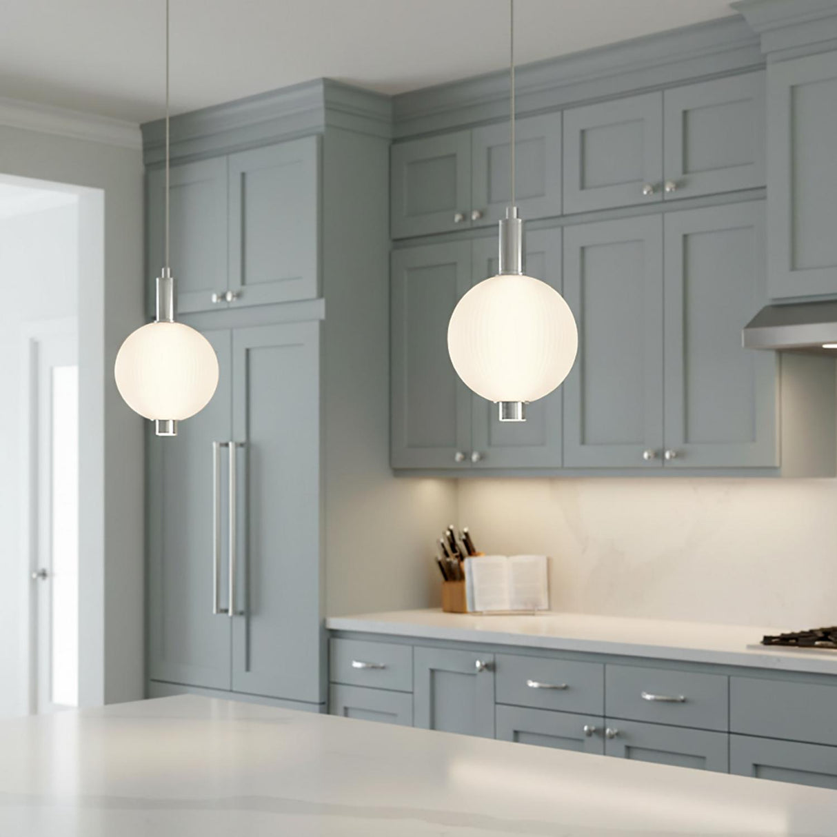 A transitional kitchen features two Nola LED Pendant 10 inch fixtures in polished nickel and ribbed opal glass hanging over a white marble island with gray cabinets.