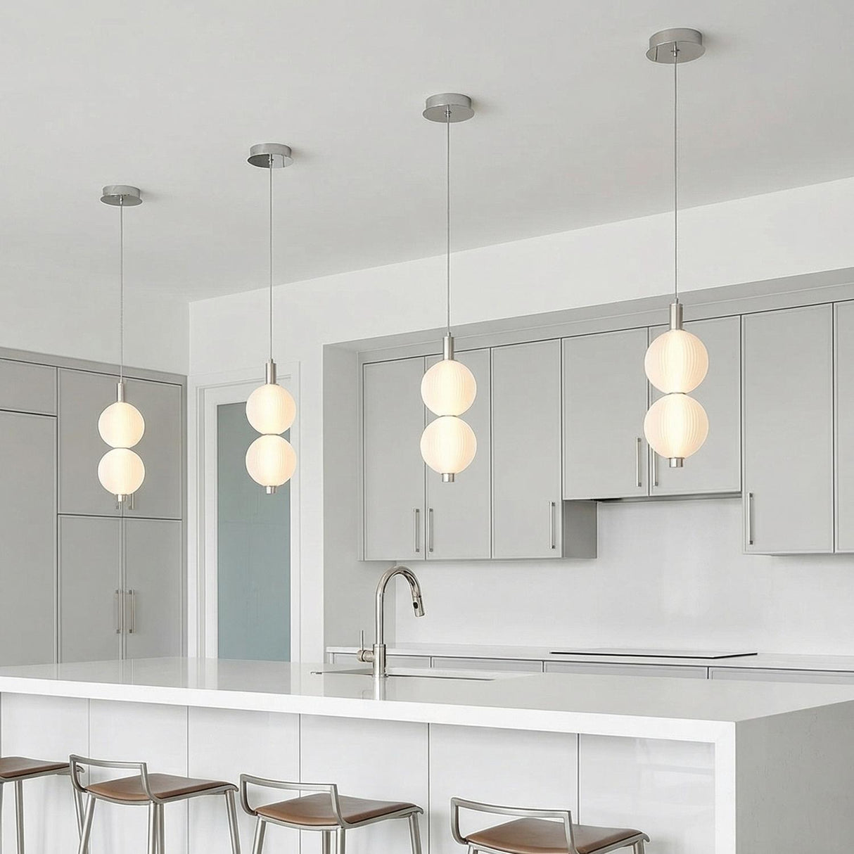 A minimalist white kitchen features four polished nickel pendants with ribbed opal glass globes over the white quartz island, gray flat-panel cabinetry, and silver bar stools.