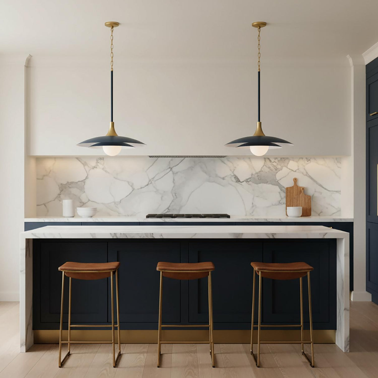 A contemporary kitchen features two Yates LED Pendant 30", Matte Navy with brushed brass accents over a marble waterfall island and navy cabinets with leather stools.