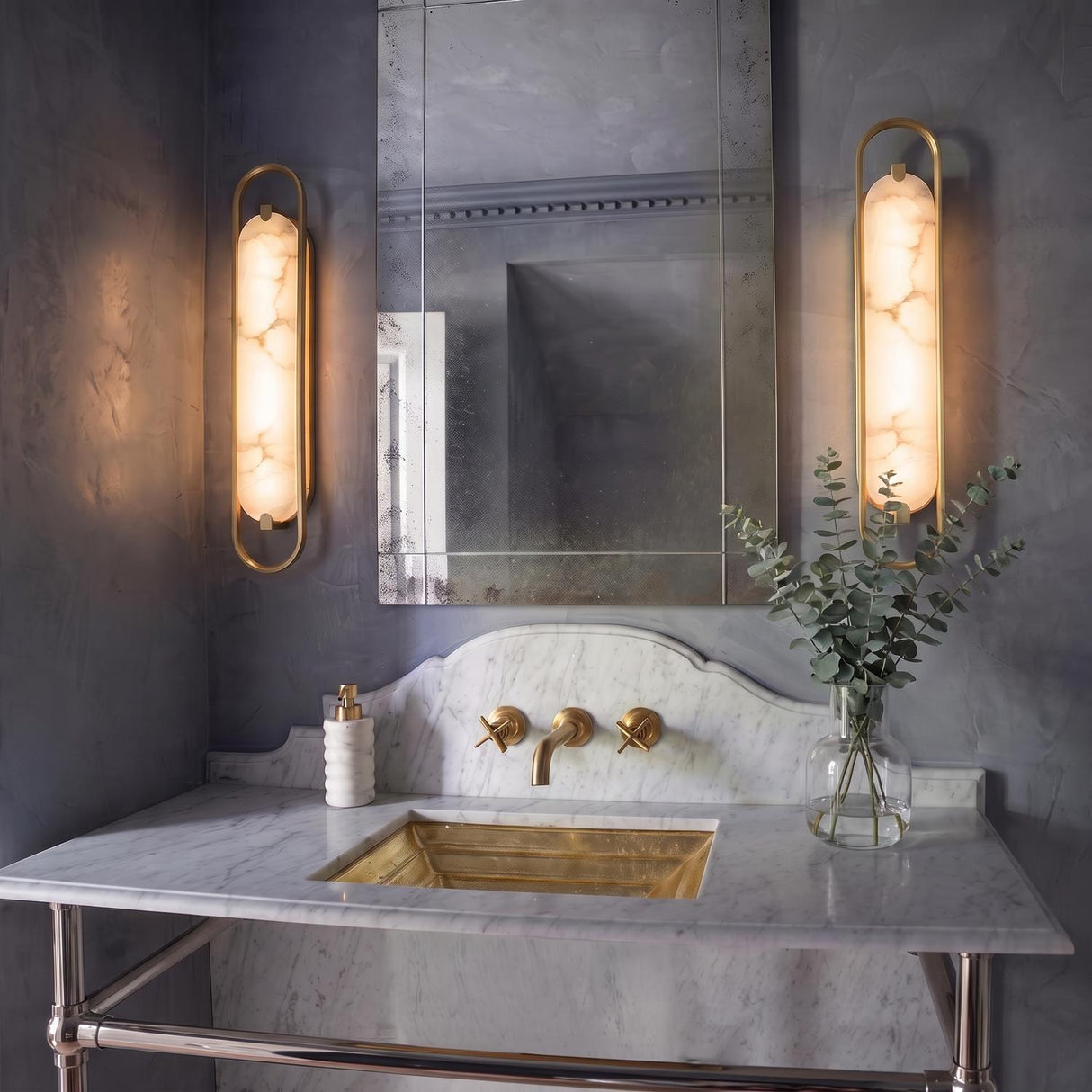 A transitional bathroom with two Inez LED Wall Sconces in brass and alabaster flanking a mirror above a marble vanity with a gold sink.