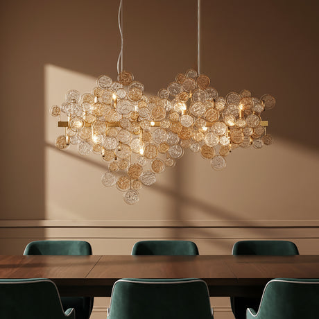 Denali 12 Light Linear 40" Chandelier, in Antique Gold with Topaz Glass, shown above a modern dining table with emerald green velvet chairs.