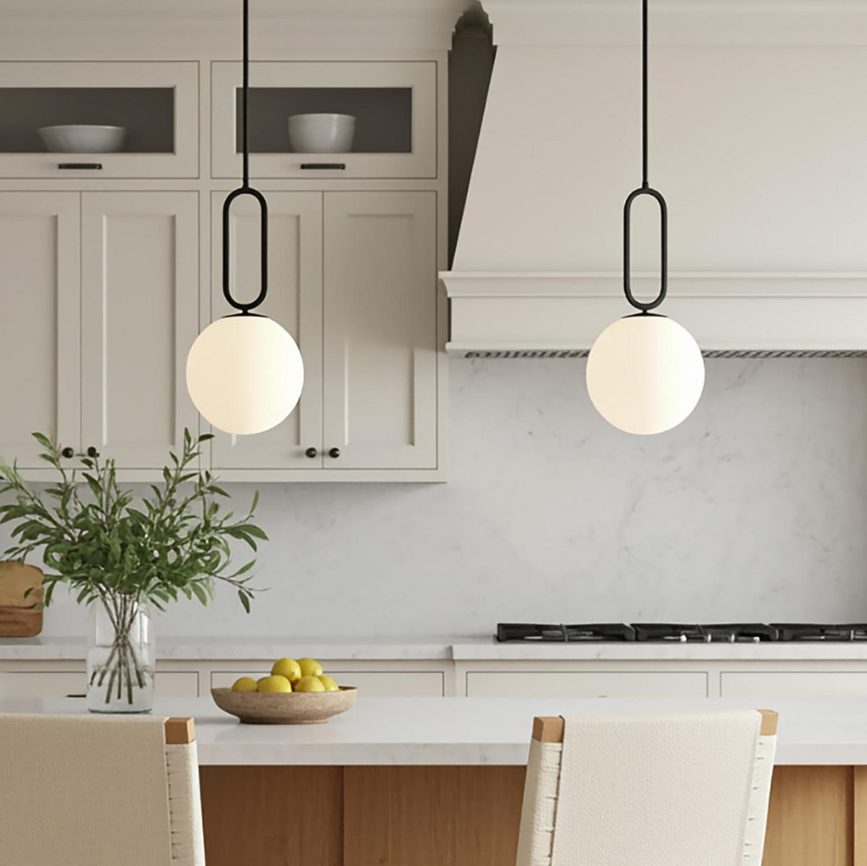 A transitional kitchen features two Oren Pendant 10", Matte Black and Opal Glass fixtures hanging over the island beside white shaker cabinets and a marble backsplash.
