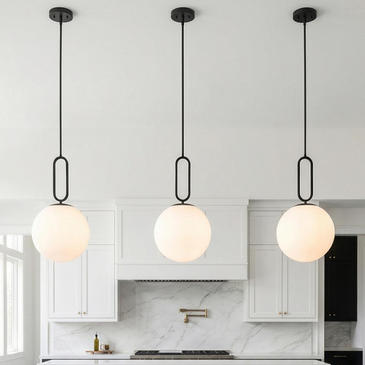 A modern kitchen features three Oren Pendant 12", Matte Black and Opal Glass fixtures over the island alongside white shaker cabinets and a marble backsplash.
