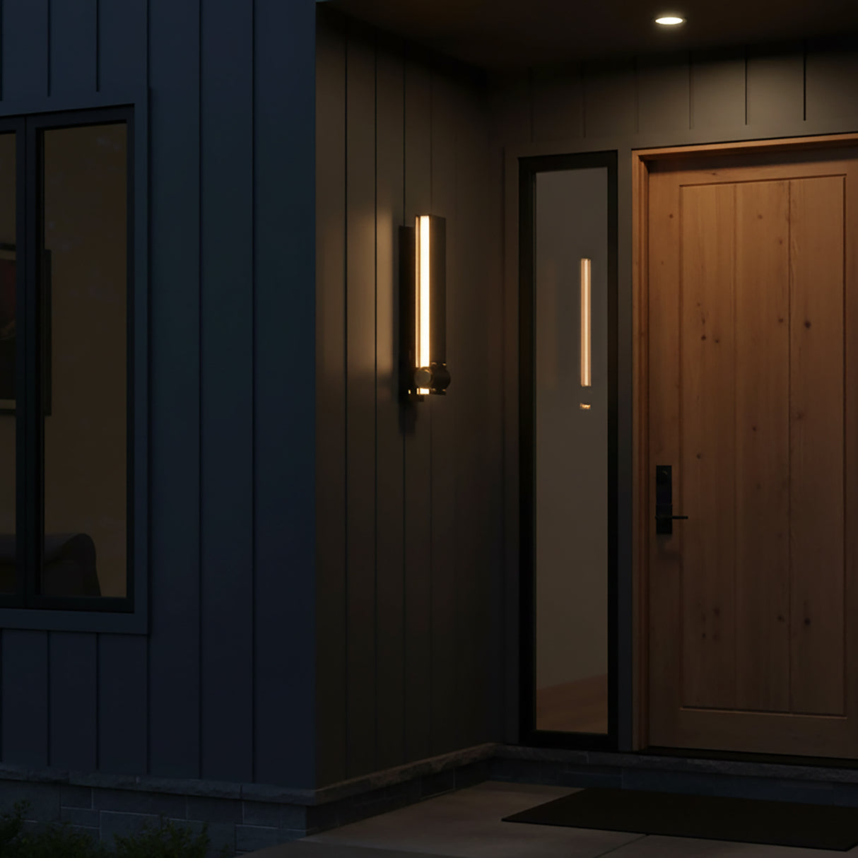 Modern house exterior with a wooden door and the Lune LED Outdoor Wall Light 19", Brass and Black, shown at night.