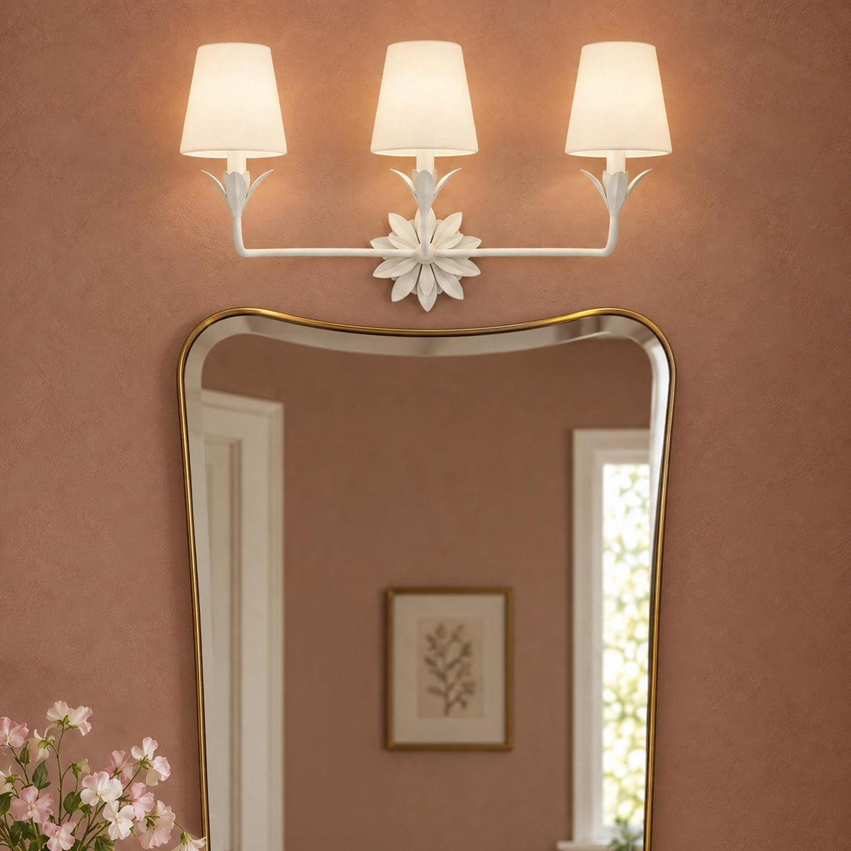 A transitional vanity area features the Ayla 3 Light Vanity, Matte White with fabric shades mounted above a brass frame mirror against warm plaster walls.