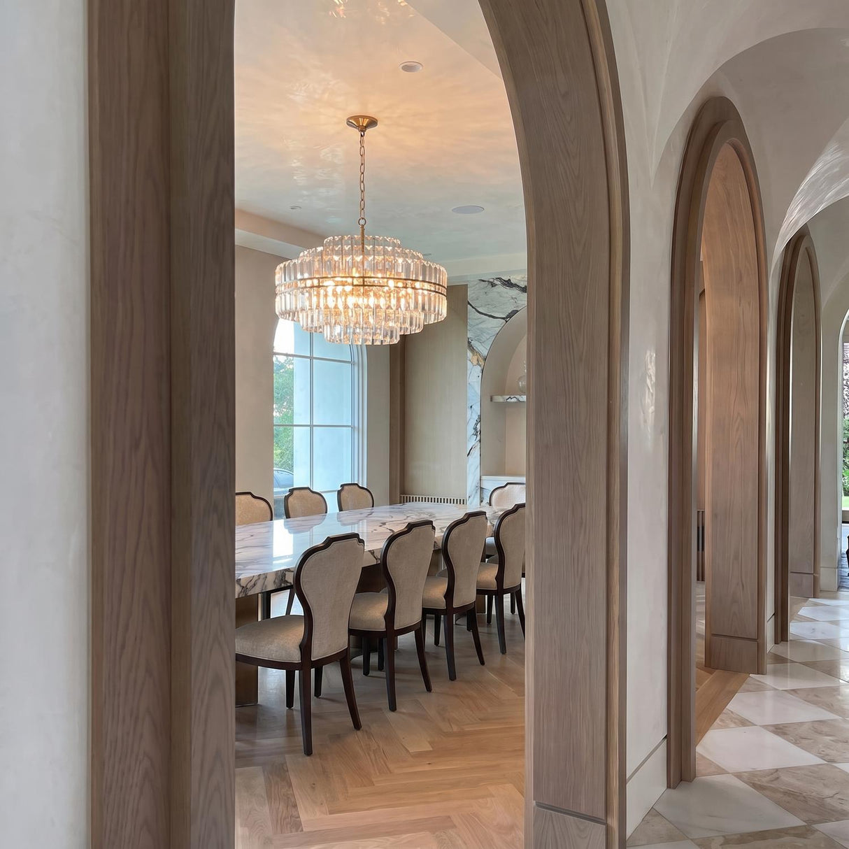 A Mediterranean dining room with the Maxwell 16 Light Chandelier 28", Crystal with Aged Brass hanging over a marble table between wooden arched doorways.