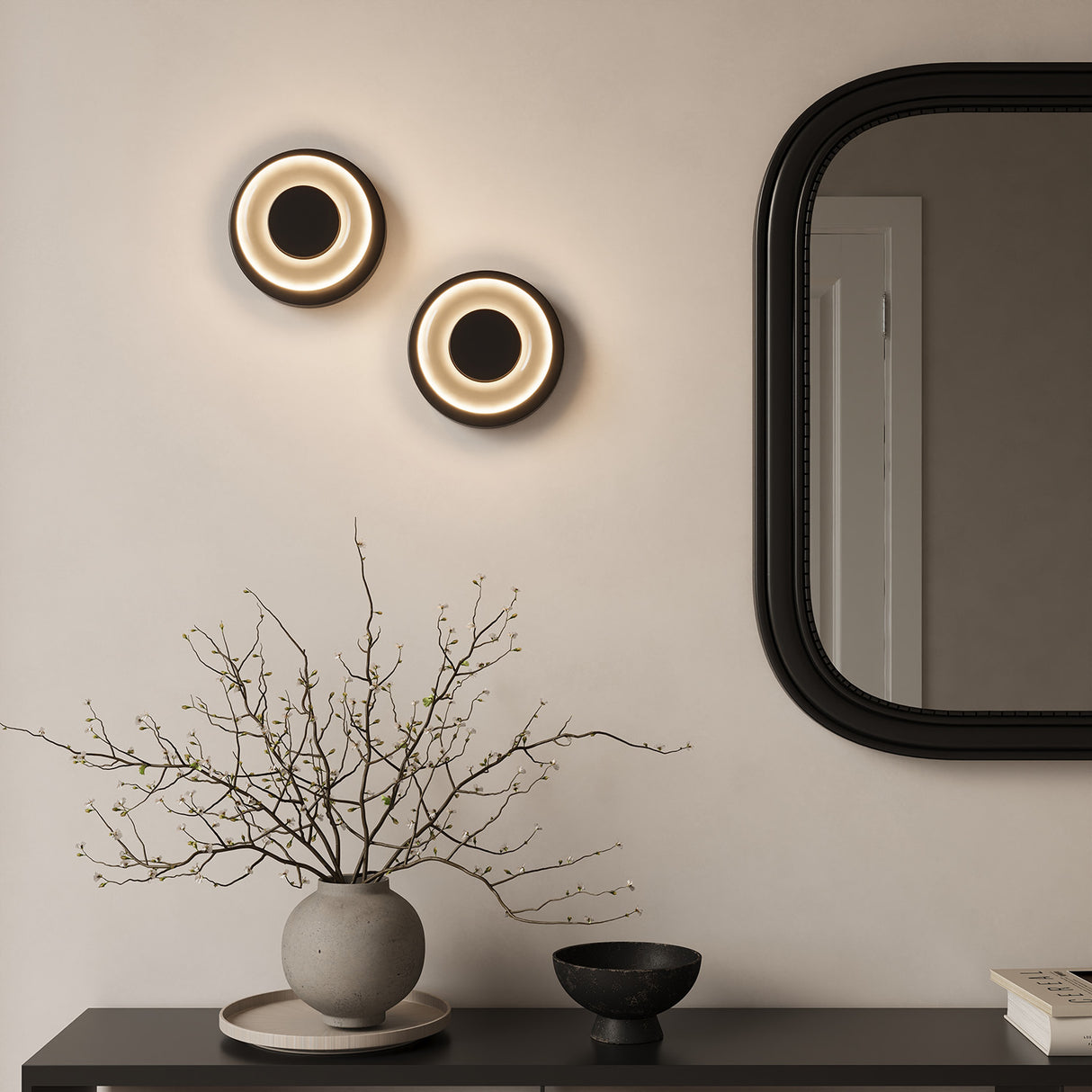 Two Cam LED Wall Sconces in Black and Frosted Glass shown above a modern console table with accessories and a black framed mirror.