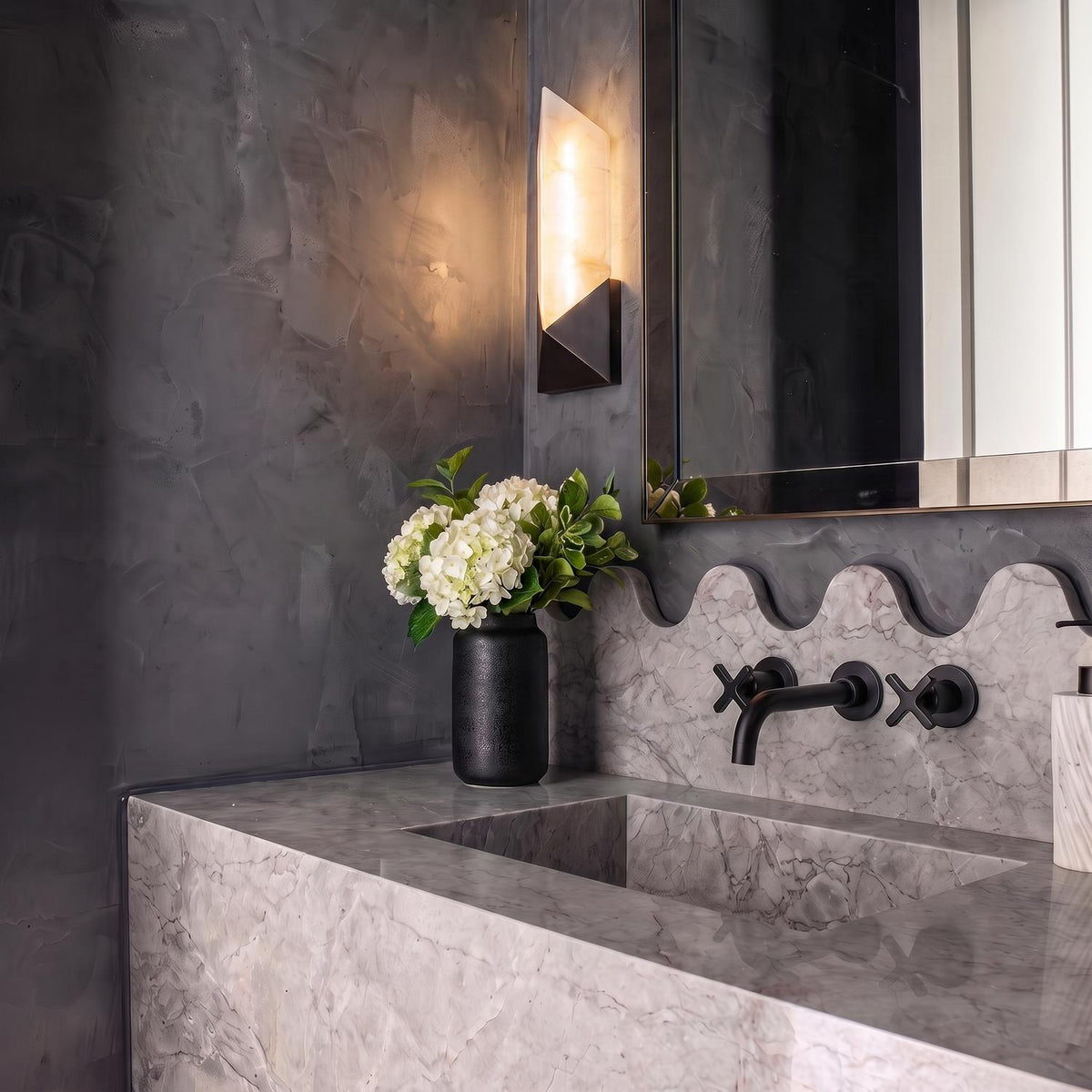 A modern bathroom with a Lunaire LED Wall Sconce in urban bronze and alabaster mounted beside a mirror above a gray marble vanity with scalloped backsplash.