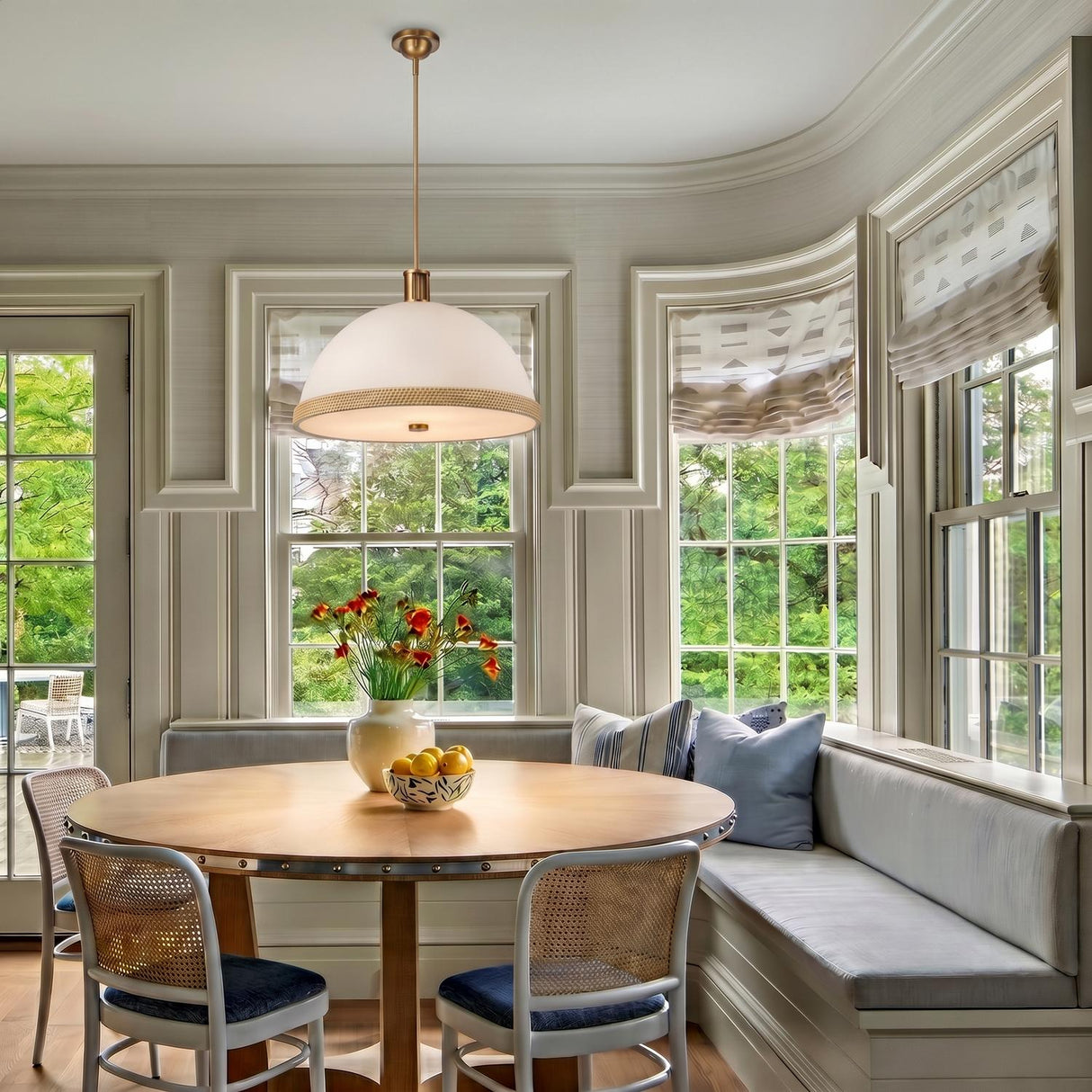 A transitional dining room with a matte white and rattan pendant over a round wood table and built-in bench seating in a sunlit bay window alcove.