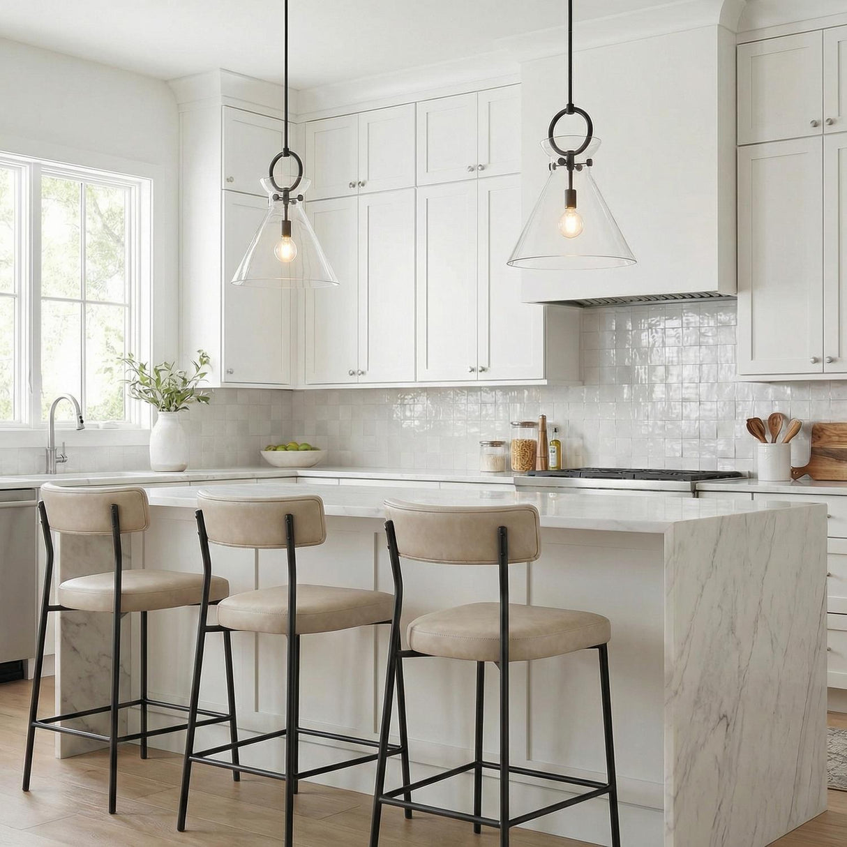 A white kitchen features two Aris Large Pendant 18", Matte Black and Clear Glass fixtures hanging over a white marble waterfall island and glossy tile backsplash.