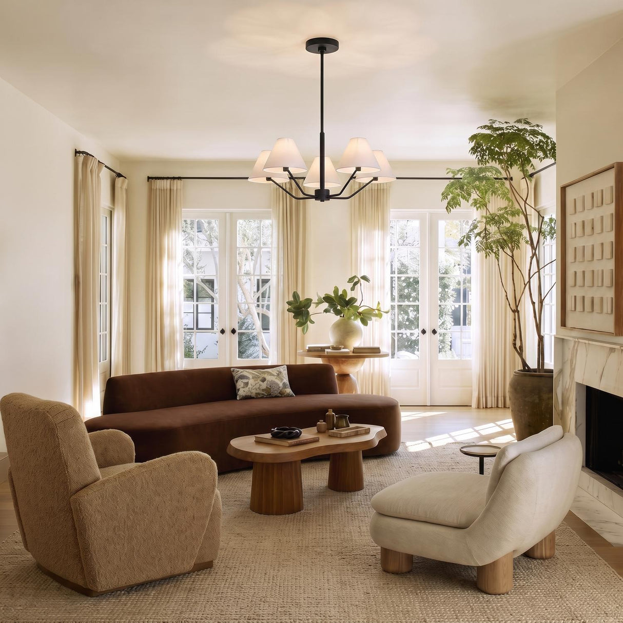 A contemporary living room featuring the Wallace 5 Light Chandelier 30 inch in matte black with white linen shades centered above a curved brown sofa near French doors.