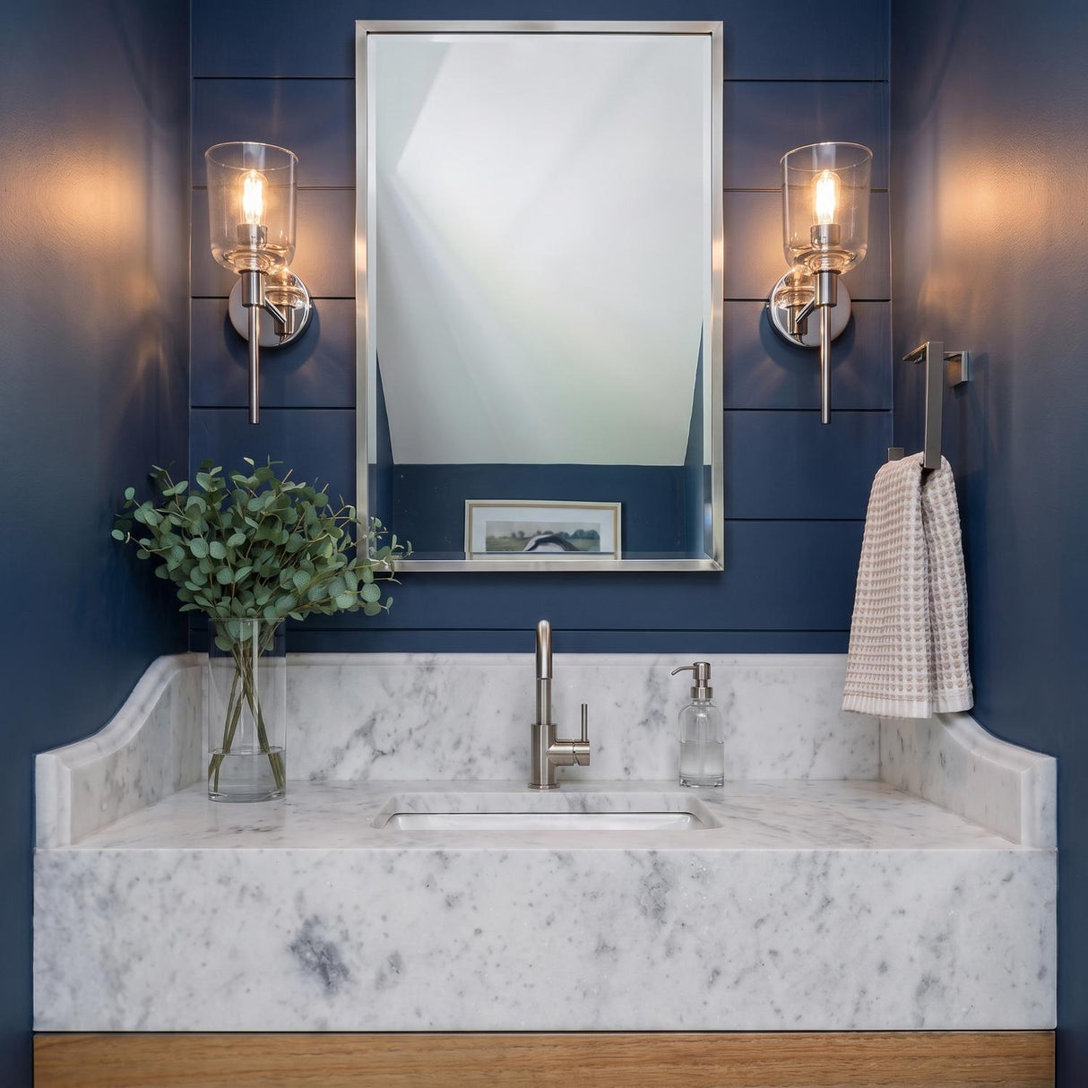 A modern farmhouse bathroom with two Emrys Wall Sconces in polished nickel flanking a mirror above a white marble vanity and navy shiplap under a sloped ceiling.