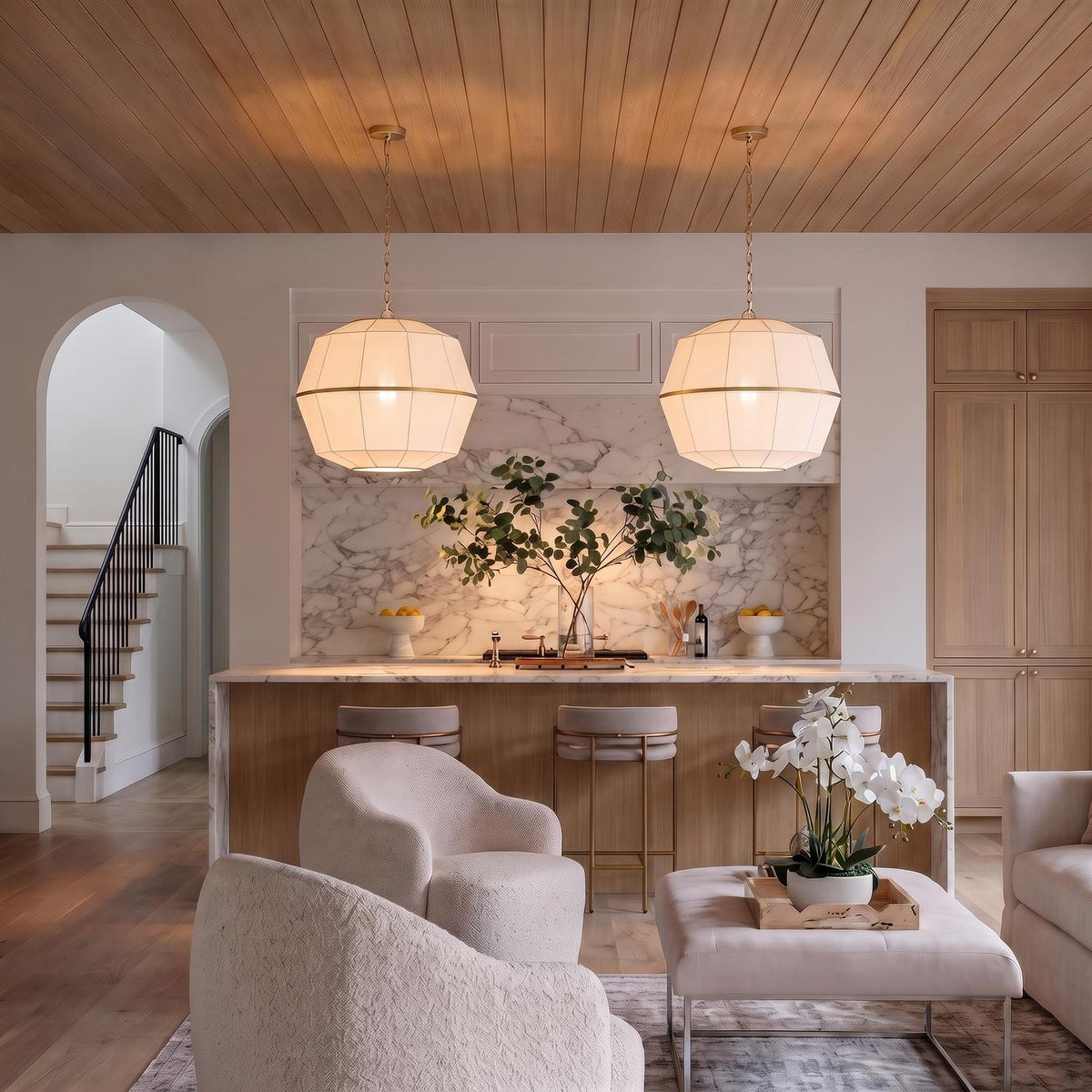 A transitional kitchen with two Birch Large Pendants in modern brass and white linen over a marble waterfall island under a light wood-slat ceiling.
