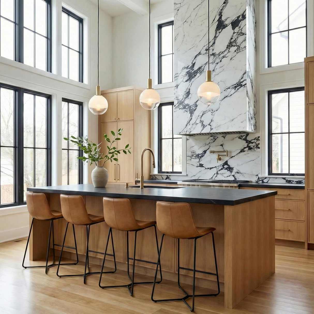 A modern kitchen featuring three Merrick Pendant 8", Modern Brass globe pendants with brushed brass hardware over a wood island with dark counters under a double-height ceiling.