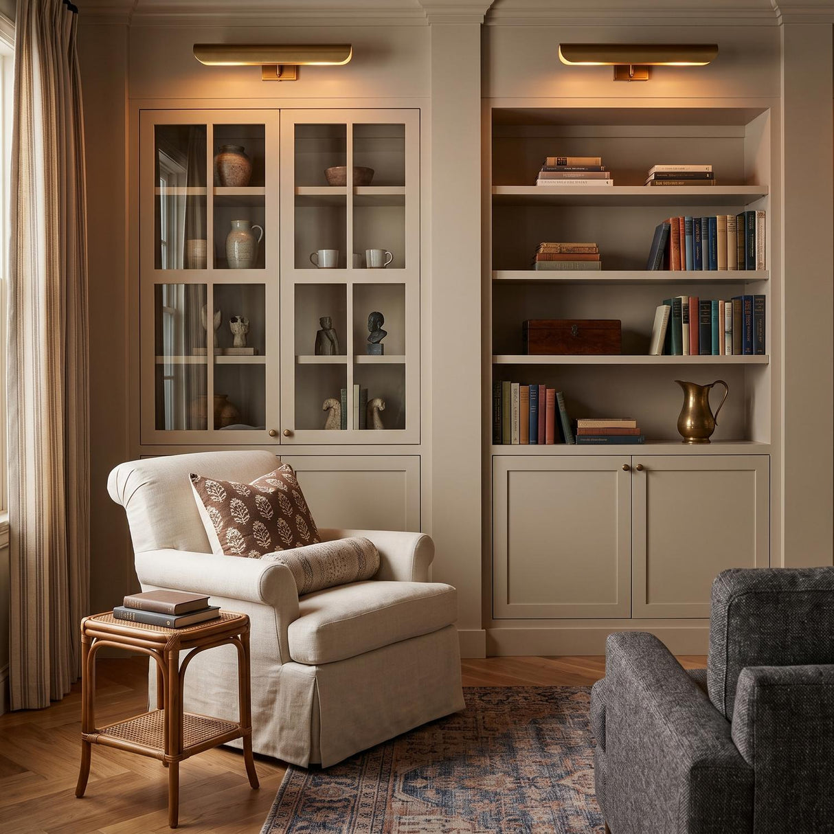 A transitional living room with two Denton Picture Light 18", Modern Brass fixtures mounted above built-in cabinetry beside a cream armchair and rattan side table.