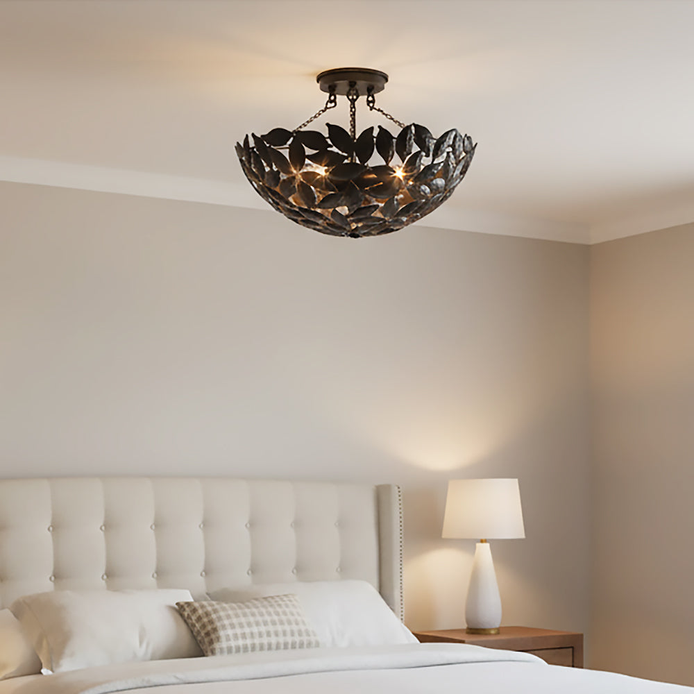 Floren Semi-Flush 16, Aged Iron - A dark, leaf-shaped semi-flush mount light fixture hangs from a ceiling above a tufted headboard and bed.