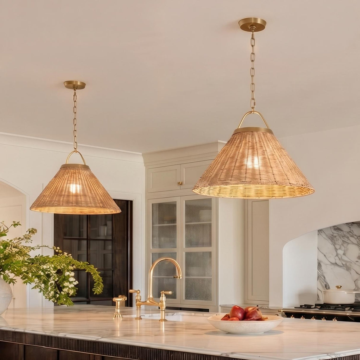 A transitional kitchen with two Paloma Pendant 22", Modern Brass and Rattan pendants over a white marble island featuring a brushed brass bridge faucet and cream cabinetry.
