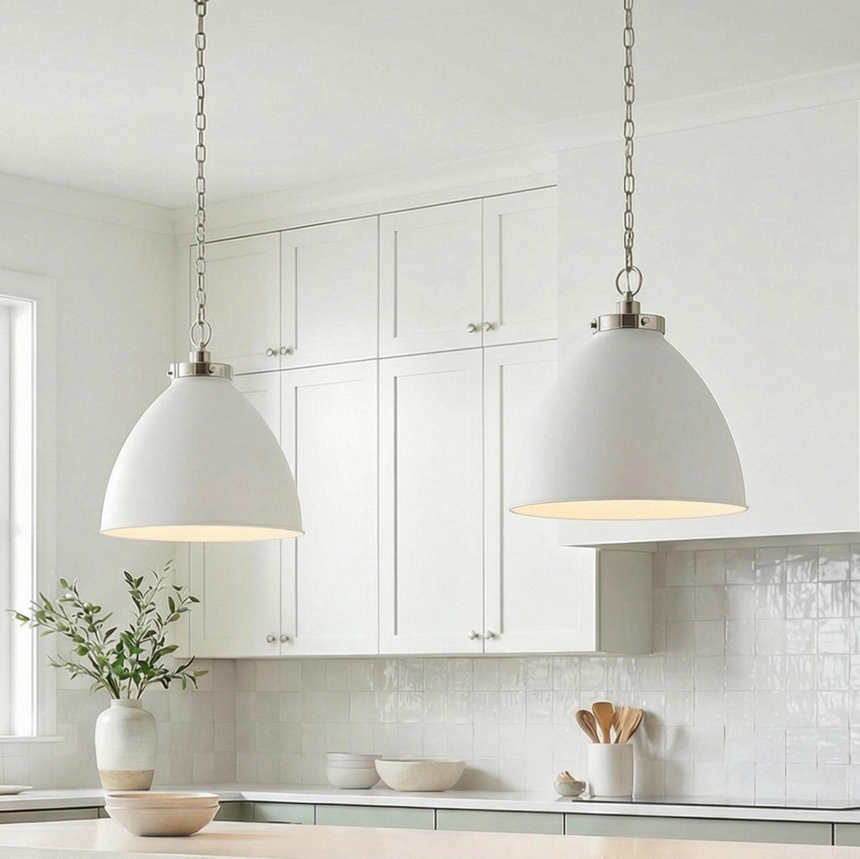 A transitional kitchen features two Rodney Large Pendant 18", Matte White and Polished Nickel fixtures over the island, alongside white shaker cabinets and a glossy tile backsplash.