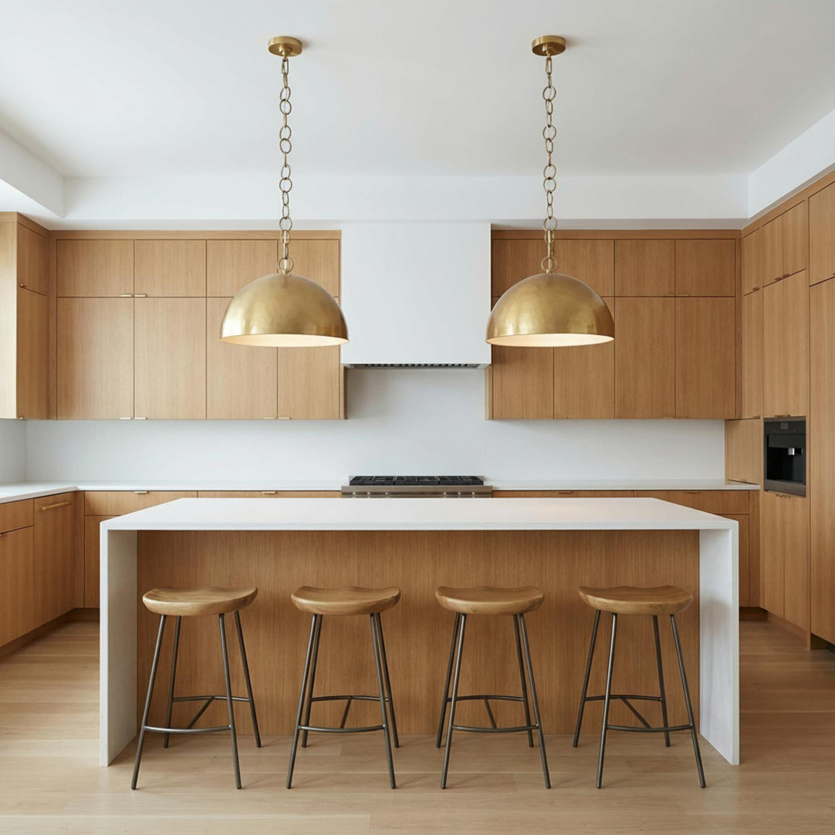 A contemporary kitchen features two Arlen Pendant 15", Modern Brass fixtures in modern brass finish over a white waterfall island with four light wood stools.